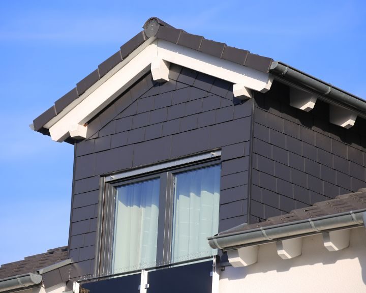 A cladded house with two windows and a black roof in the city.